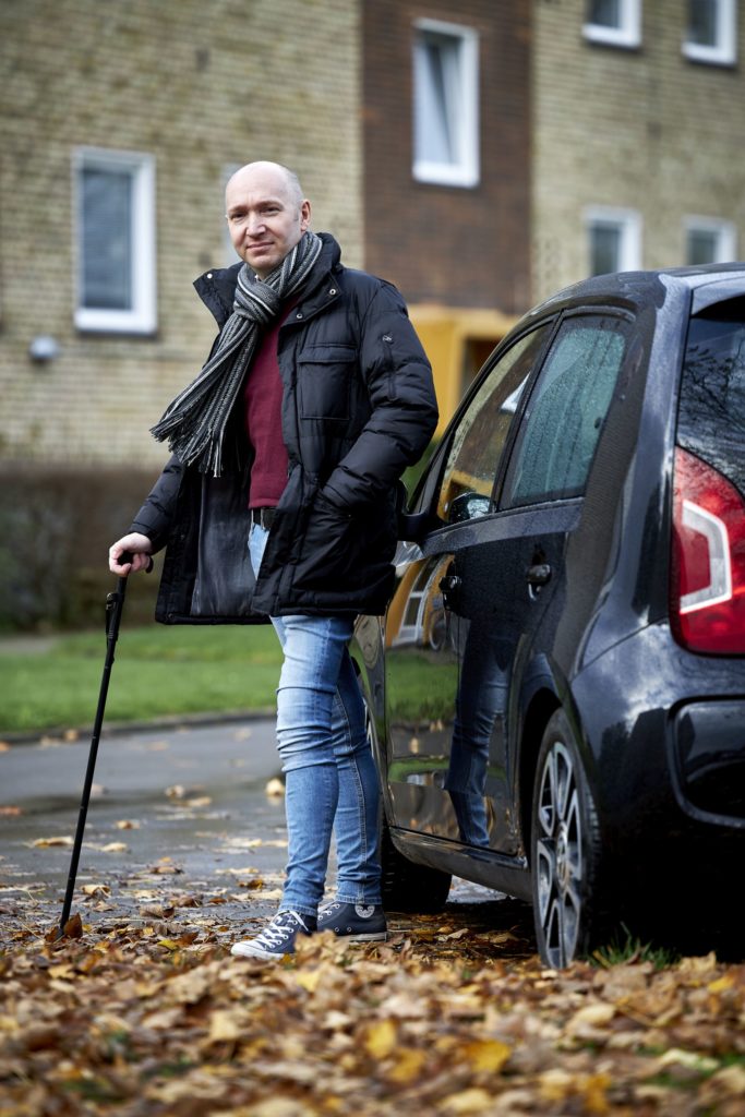 Mand med stok står ved sort bil.